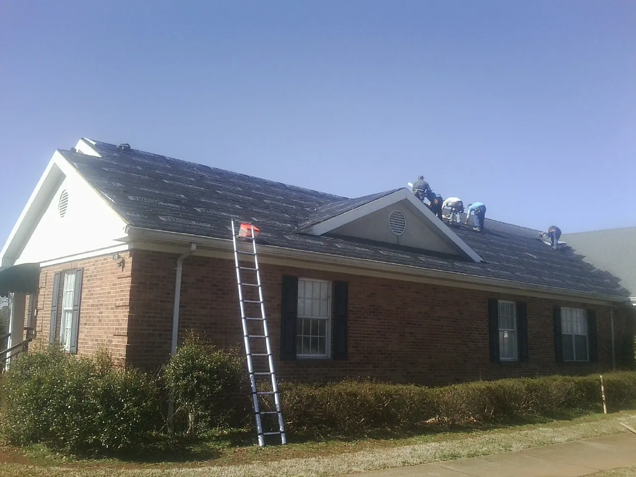 Crew tearing shingles off a brick ranch roof with a ladder set — Emergency Roof Repair work by our crew in Van Wert