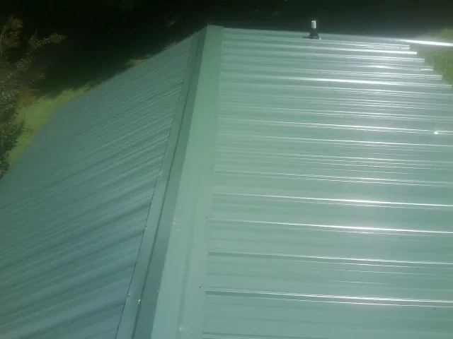 New green metal panels meeting at the ridge of a roof — Flat Roof Repair work by our crew in Van Wert