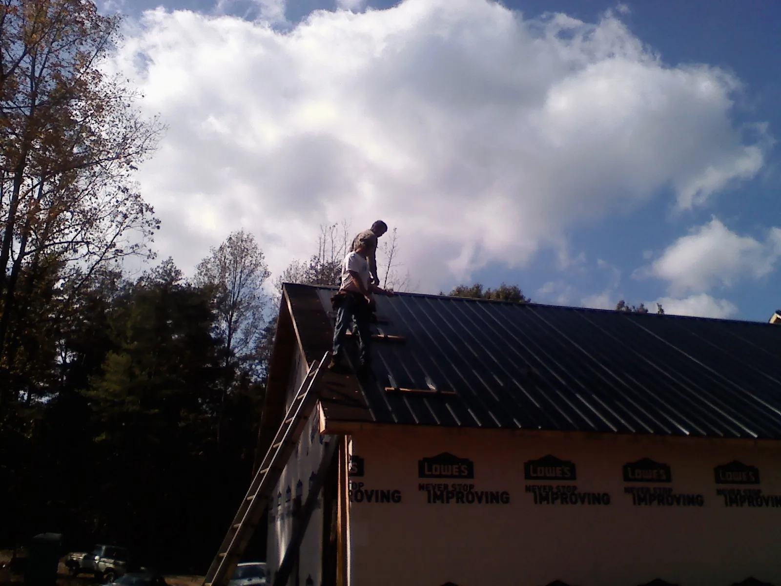 Roofer fastening dark metal panels high against a cloudy sky, from a Roof Inspection job in Van Wert